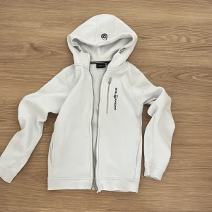 Vit hoodie från Sail Racing med dragkedja - Vit hoodie från Sail Racing med hel dragkedja framtill och en extra bröstficka med dragkedja. Tröjan har broderad logga på bröstet och en skön huva. Perfekt för dig som gillar sportig och clean stil. Säjer denna för jag har växt ur den. Köpte denna för 999kr och säljer den för 349+frakt nu. Den är i bra skick och har storlek 150 cm. Hör av er vid frågor pris kan även diskuteras😊
