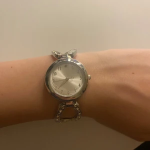Silverfärgad klocka med glittrande detaljer - Mycket elegant klocka, armbandet har snygga glittrande stenar och en unik form som ger ett elegant intryck. Perfekt accessoar för att lyfta din outfit med lite extra bling. Batteri funkar ej och måste bytas (ingår ej)