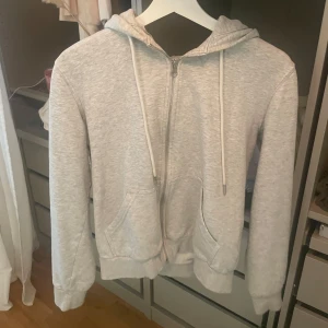 Ljusgrå hoodie med dragkedja - En basic ljusgrå hoodie med dragkedja framtill och huva med snörning. Tröjan har två fickor på magen och ribbade muddar vid ärmslut och nederkant. 🩶🩶🤍🤍