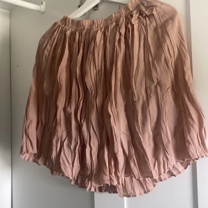 Beige plisserad kortkjol från NA-KD - Supersöt beige plisserad kortkjol från NA-KD i storlek 34. Kjolen har en creased effekt och elastisk midja som gör den bekväm och lätt att bära. Perfekt att styla med en enkel topp och sneakers för en chill look.