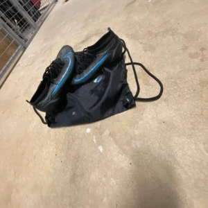 Nike svarta fotbollsskor med blå detalj Nike mercurial Vapor 14 Elite - Säljer ett par svarta Nike fotbollsskor med blå swoosh och snygga detaljer. Skorna har snörning och platt sula med dobbar för bra grepp på planen. Ovandelen är i syntetmaterial och designen är smal och sportig. Perfekta för dig som vill sticka ut på fotbollsplanen.