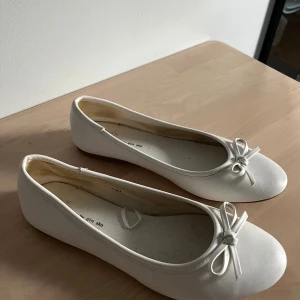 Vita ballerinaskor med rosett från Din Sko - Snygga vita ballerinaskor från Din Sko i storlek 36. Skorna har en klassisk rund tå, platt sula och en söt rosettdetalj framtill. Använda fåtal gånger och har endast tecken på användning inuti skorna.