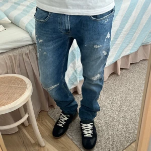 Blå Replay anbass jeans med slitningar - Säljer ett par blå jeans från Replay med coola slitningar och distressed detaljer framtill. Jeansen har klassisk femficksdesign, normal passform och raka ben. Perfekta för dig som gillar en avslappnad och trendig look.