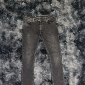 Grå jeans från Nudie Jeans W32 L34 - Snygga grå jeans från Nudie Jeans med klassisk femficksdesign och ikonisk broderad bakficka. Jeansen har en rak passform och är tillverkade i mjukt denimtyg. Perfekta för dig som gillar en stilren och avslappnad look.
