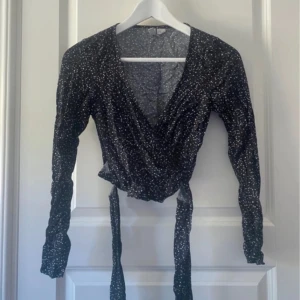 Omlottoppar med hjärtmönster H&M Divided - Två omlottoppar från H&M Divided i storlek 34. En svart med vita små hjärtan och en vit med svarta hjärtan. Båda har långa ärmar, knytband i midjan och djup v-ringning. Perfekta för dig som gillar söta detaljer och vill ha en feminin look.