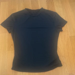 Svart basic t-shirt med kort ärm - En stilren svart t-shirt med korta ärmar och rund hals. Modellen är figurnära och passar perfekt till jeans eller kjol. Enkel och klassisk design utan tryck eller mönster, vilket gör den lätt att matcha med allt.