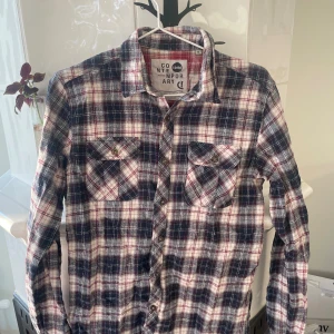 Rutig skjorta - Säljer en rutig skjorta från Solid Contemporary i storlek M men sitter som S. Skjortan har blå, röda och vita toner, två bröstfickor med knappar och klassisk krage. Perfekt för dig som gillar en avslappnad och snygg stil.