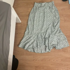 Ljusgrön blommig långkjol med volang - Supersöt ljusgrön långkjol med vitt blommönster och volang nertill. Kjolen har en flowy passform och är perfekt för vår och sommar. Ingen synlig dragkedja eller knappar, bara ett härligt fall och mjukt material.