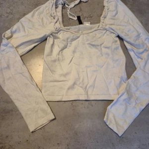 Vit långärmad topp från H&M Divided - Säljer en vit långärmad topp från H&M Divided i storlek XS. Toppen har en fyrkantig ringning med knytband upptill och är croppad i modellen. Perfekt att styla med jeans eller kjol för en trendig look.
