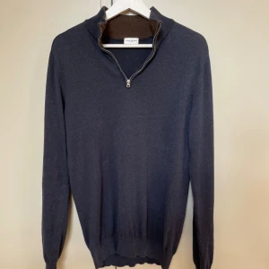 Mörkblå stickad tröja från John Henric - Snygg mörkblå stickad tröja från John Henric med ribbad krage och half zip-dragkedja. Insidan av kragen är brun för en schysst kontrast. Tröjan har långärmad passform och är tillverkad i mjuk bomull som känns skönt mot huden.