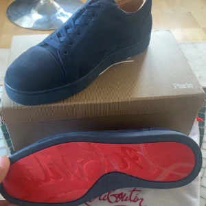 Mörkblå Christian Louboutin - Snygga mörkblå sneakers från Christian Louboutin i mocka med klassisk röd sula och ton-i-ton broderad logga på hälen.  Skorna är använda 1 gång men inga defekter eller liknande. Storlek 43