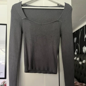 Grå ribbad topp från Gina Tricot - Säljer en grå ribbad långärmad topp från Gina Tricot. Toppen har en snygg v-ringad skärning och sitter figurnära. Perfekt att styla med jeans eller kjol för en clean look. Materialet är stretchigt och bekvämt.
