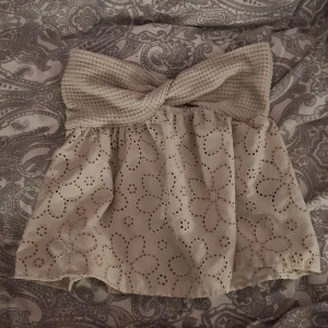 Beige topp med broderade blommor från SHEIN - Supersöt beige topp från SHEIN med broderade blommor och hålmönster. Toppen har en stickad, twistad midja som ger en unik look och sitter bekvämt. Perfekt för dig som gillar romantiska och feminina detaljer.