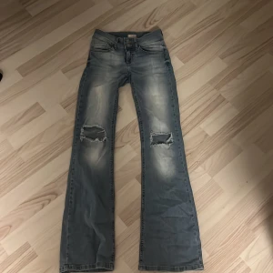 Blå bootcut jeans från Nelly - Snygga blå bootcut jeans från Nelly, strl 34. med slitna detaljer och hål på båda knäna. Jeansen är i mycket bra skick och säljes pgr av för korta i benen.