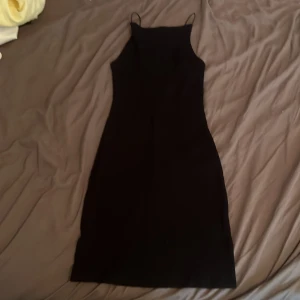 Svart klänning  - Säljer en svart, ribbad klänning med smala axelband och rak halsringning. Klänningen är kort och har en tight passform som framhäver figuren. Perfekt för dig som gillar minimalistisk stil och vill ha något enkelt men snyggt. Materialet känns mjukt och stretchigt. Sedan på ryggen har den en liten u ringad öppning. Det står ej vilken storlek, men skulle säga den passar xs, s, m