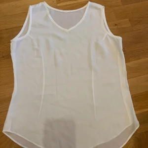 Vit ärmlös linnetopp med v-ringning - Vit linnetopp med v-ringad hals och ärmlös design.  