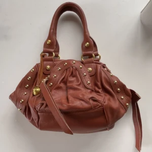 Brun/burgundy vintage väska😩🍂🍒 - Säljer en brun/burgundy vintage handväska i skinn med coola guldfärgade nitar o så skit snygga detaljer! Kommer tyvärr inte till användning. Kommer även med ett längre band, som är lite slitet men fungerar, resten av väskan är i superbra skick😉💖