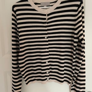 Randig kofta från H&M i svart och vitt - Säljer en snygg randig kofta från H&M i svart och vitt. Koftan har rund halsringning, knäppning framtill med vita knappar och långa ärmar. Perfekt att slänga på sig över en t-shirt eller linne. Materialet är mjukt och skönt, troligtvis bomull eller en bomullsblandning.Helt ny utan prislapp💕