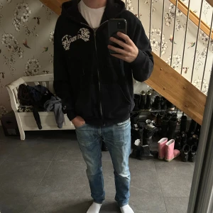 Svart Champion hoodie med tryck - En skit snygg vintage svart hoodie från Champion med vit text på bröstet och stort tryck på ryggen. Dragkedja framtill, huva med snörning och kängurufickor. Skön och avslappnad passform, perfekt för chill dagar. Tillverkad i mjuk bomullsblandning.