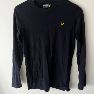 Mörkblå långärmad tröja Lyle & Scott - Snygg mörkblå långärmad tröja från Lyle & Scott Junior. Tröjan har rund halsringning och den klassiska gula loggan broderad på bröstet. Tillverkad i 100% bomull, perfekt för en clean och stilren look.