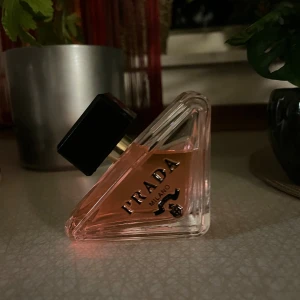 Prada Parfym paradoxe  - Snygg parfym från Prada med unik trekantig glasflaska och svart fyrkantigt lock. Vätskan är ljusrosa och flaskan har tydlig Prada-logga i svart. Lyxig design som sticker ut på hyllan och passar dig som gillar exklusiva dofter.