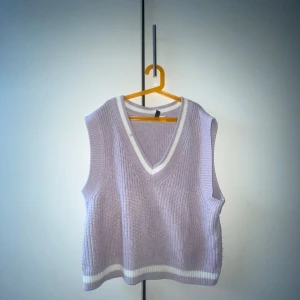 Ljuslila stickad väst från H&M Divided - Superfin ljuslila stickad väst från H&M Divided i storlek M. Västen har v-ringning och vita ribbade detaljer vid halsringning och nederkant. Perfekt att styla över en skjorta eller t-shirt för en trendig look.