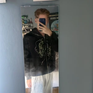 Svart hoodie med strassmotiv från SHEIN - Svart hoodie från SHEIN i storlek L/Mmed hel dragkedja och huva. Framsidan har coola strassmotiv i form av ansikten och text. Hoodien är i syntetmaterial och har en relaxed passform med långa ärmar. Perfekt för dig som gillar streetstyle och unika detaljer.