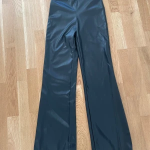 Svarta vida byxor i skinnimitation - Snygga svarta byxor i skinnimitation med Bootcut modell och midwaist. Små i storleken 