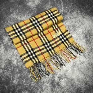 Rutig halsduk från Burberry i ull - Klassisk halsduk från Burberry med ikoniskt rutigt mönster i beige, svart, vitt och röda detaljer. Gjord i 100% lammull och har snygga fransar i ändarna. Perfekt accessoar för att lyfta din stil med brittisk elegans.