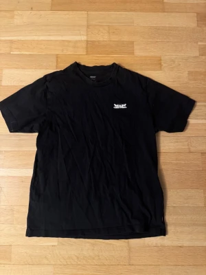 Svart Levi's t-shirt med tryck - Svart t-shirt från Levi's i relaxed fit med vit tryckt logga på bröstet och stort grafiskt tryck med text på ryggen. Klassisk rund hals och korta ärmar. Materialet är mjuk bomull som känns skönt mot huden. Perfekt för dig som gillar streetwear och tydliga prints.