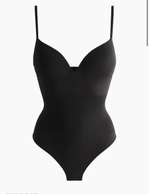 Svart body med smala axelband - Snygg svart korsett-topp med smala axelband och v-ringad front. Toppens form ger en markerad midja och en tight passning som framhäver siluetten. Perfekt att styla med jeans eller kjol för en trendig look.