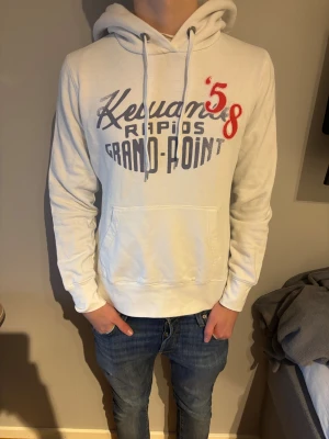 Vit hoodie med tryck 'Kewaunee Rapids 58' - Säljer en vit hoodie. Framsidan har ett coolt tryck i blått och rött med texten 'Kewaunee Rapids Grand-Point' och siffran 58. Mjuk bomullskänsla, perfekt för chill dagar. Långärmad och med dragsko vid huvan.