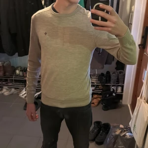 Morris tröja med broderad detalj - Säljer en stilren beige tröja med en liten broderad detalj på bröstet. Tröjan har långa ärmar och en rund halsringning. Perfekt för en avslappnad look.