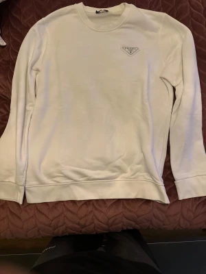 Vit långärmad tröja från Prada - Snygg vit långärmad tröja från Prada med rund hals och diskret logga på bröstet. Tröjan har en clean och stilren look, perfekt för dig som gillar minimalistisk design. Tillverkad i mjukt material som känns skönt mot huden.