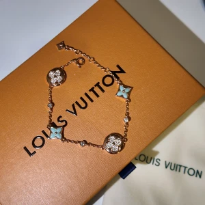 Louis Vuitton armband med blommor - Lyxigt armband från Louis Vuitton i roséguld med ikoniska LV-blommor och stjärnor. Dekorerat med ljusblå emalj och gnistrande stenar, samt LV-logga på baksidan av berlockerna. Kedjan är tunn och elegant, perfekt för att lyfta din outfit.