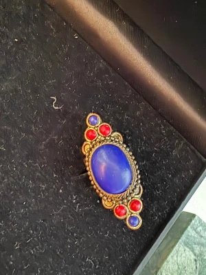 Statementring med blå och röda stenar - Unik statementring med en stor oval blå sten i mitten och mindre runda röda och blå stenar runtom. Ringen har en antikguldig metallbas med detaljerad kant och justerbar ringdel. Perfekt för dig som gillar färgstarka accessoarer och vintagevibbar.