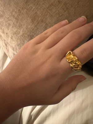 Chunky guldpläterad ring med organisk form - Säljer en chunky ring i guldpläterad metall med cool, organisk och skulpterad design. Ringen har en unik, vågig yta som ger den en edgy och modern vibe. Perfekt för dig som gillar statement-smycken och vill sticka ut med något annorlunda.