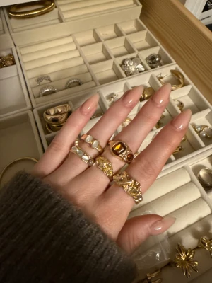 Fem chunky ringar i guld och pärlemor - Säljer ett set med fem chunky ringar i guldton, två med pärlemordetaljer och en med bruna stenar. De har en cool, organisk form och passar perfekt för dig som gillar statement-smycken. Ingen märkning syns på ringarna.