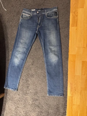 Blå Replay grover jeans slimfit - Snygga blå Replay Anbass jeans med slimfit och klassisk femficksdesign. Jeansen har ljusa slitningar framtill och coola detaljer på bakfickorna. Perfekt passform och stretchigt jeanstyg som sitter tajt och bekvämt hela dagen.