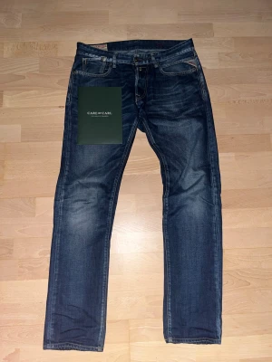 Replay jeans blå straight fit 32/34 - Snygga blå jeans från Replay i klassisk straight fit med kontrastsömmar och fem fickor. Jeansen har en mörk tvätt med lätt slitning och detaljerad Replay-logga vid fickan. Perfekt passform.