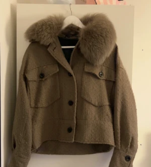 Meotine beige pälskappa  - Säljer en beige pälsjacka från meotine med superfluffig krage i pälsimitation. Jackan är croppad, har stora fickor med knappar framtill och grov textur i tyget. Insidan är fodrad med slätt, mörkt tyg. Perfekt för dig som vill ha en statementjacka med cool vintage vibe.