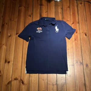  Vintage Mörkblå pikétröja Polo Ralph Lauren - Snygg mörkblå pikétröja från Polo Ralph Lauren med klassisk krage, broderad logga på bröstet och coola detaljer som FRANCE 012 på ryggen. Tröjan är i bomull och har korta ärmar, perfekt för en sportig och stilren look. Kom gärna med frågor och pruta för en snabb affär storlek xl i barn storlek 18-20 år 