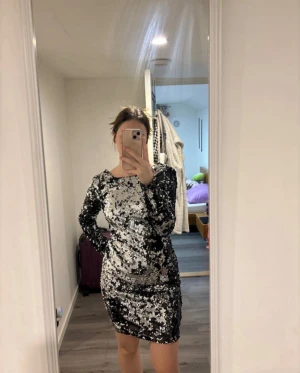 Paljettklänning i svart och silver S - Säljer en kort, glittrig klänning i svart och silver med paljetter över hela. Klänningen har långa ärmar och en djup, öppen rygg som ger en riktigt snygg look. Tight passform och rund halsringning framtill. Perfekt för dig som vill sticka ut och har pris lapp på.
