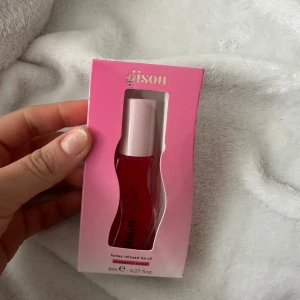 Gisou Honey Infused Lip Oil Strawberry Sorbet - Säljer en Gisou honey infused lip oil i färgen Strawberry Sorbet. Läppoljan kommer i en snygg, vågformad transparent flaska med rosa lock och har en intensiv röd nyans. Innehåller 8 ml och ger glans och fukt till läpparna med en hint av honung.
