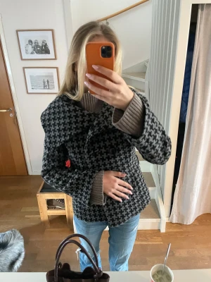 unik grå-svart rutig skepparkavaj - Säljer en grå och svart skepparkavaj med stort krage och dubbelknäppning. Jackan har ett klassiskt rutigt mönster i hundtandsstil och är i tjockt, mjukt material som känns ulligt. Perfekt till höst och vinter för en stilren look.