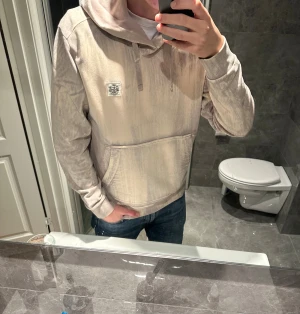 Beige hoodie från Stone Island - Säljer en riktigt schysst hoodie från Stone Island med snygg beige tvätt. Hoodien är i storlek M och jag på bilden är 188cm. Hoodien är så gott som oanvänd och har inga tecken på användning. Hör av er vid funderingar:)