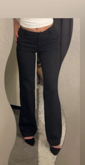 Svarta bootcut kostymbyxor - Snygga svarta kostymbyxor med bootcut passform och klassiska bälteshällor. Byxorna har en rak siluett upptill och blir vidare nedtill, vilket ger en trendig look. Perfekta att matcha med crop top eller skjorta. Materialet känns mjukt och har en lätt stretch.