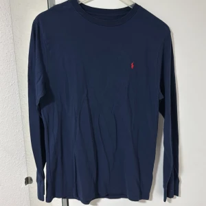Marinblå långärmad tröja Polo Ralph Lauren - Snygg marinblå långärmad tröja från Polo Ralph Lauren i mjuk bomull. Klassisk rund hals och diskret röd logobrodyr på bröstet. Storlek XL