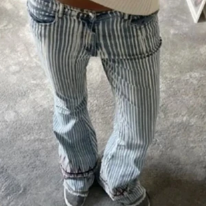 Randiga jeans i blått och vitt - Snygga randiga jeans i blått och vitt med en bootcut-sti och låg midjal. De har en klassisk femficksdesign och en knappgylf. Perfekta för en avslappnad look med en twist. Har sytt om dem själv!!!🩷 första 2 bilderna lånade!!Midjemått rakt över är 40cm och innerbenslängden är 82cm❤️