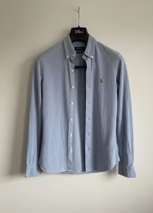  Polo Ralph Lauren skjorta ljusblå i S - Snygg ljusblå skjorta från Polo Ralph Lauren med klassisk krage och broderad logga på bröstet. Skjortan har lång ärm, knappar framtill och är tillverkad i mjuk bomull. Perfekt för dig som gillar stilrena och tidlösa plagg med en exklusiv touch. Inte defekter förutom en knapp vid ärmen som är borta, därav prisminskningen🙌😇
